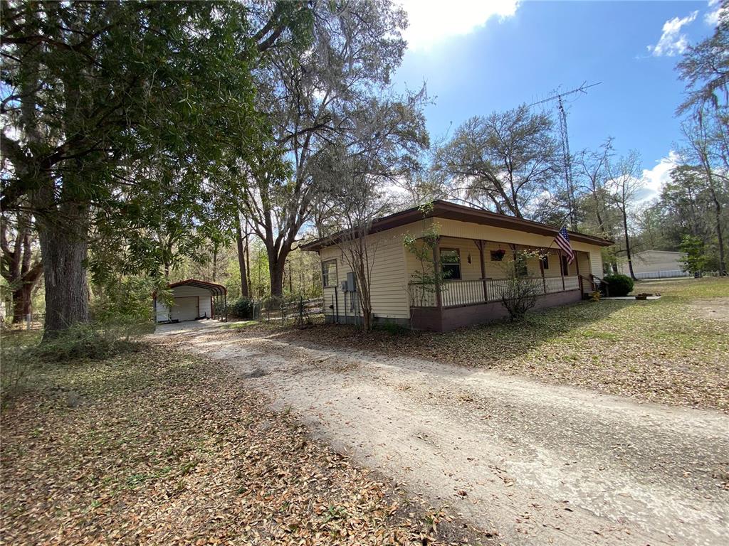 A single-story house with a front porch and a detached carport sits on a wooded lot — 15213 NW 31ST TERRACE, GAINESVILLE, FL
