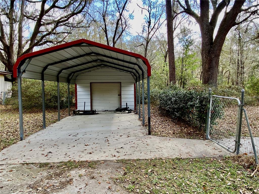 A metal carport with a red roof stands over a concrete slab in a wooded area — 15213 NW 31ST TERRACE, GAINESVILLE, FL