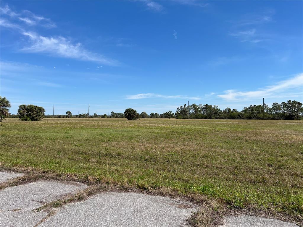 A flat, grassy vacant lot is viewed from the edge of a paved road — 12386 GREENLING WAY, PLACIDA, FL