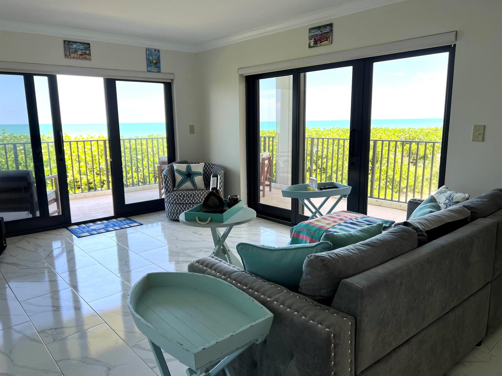 A living room with tile floors, a grey sofa, and sliding glass doors overlooking the ocean — 7420 S Ocean Drive # 216, Jensen Beach FL 34957, JENSEN BEACH, FL