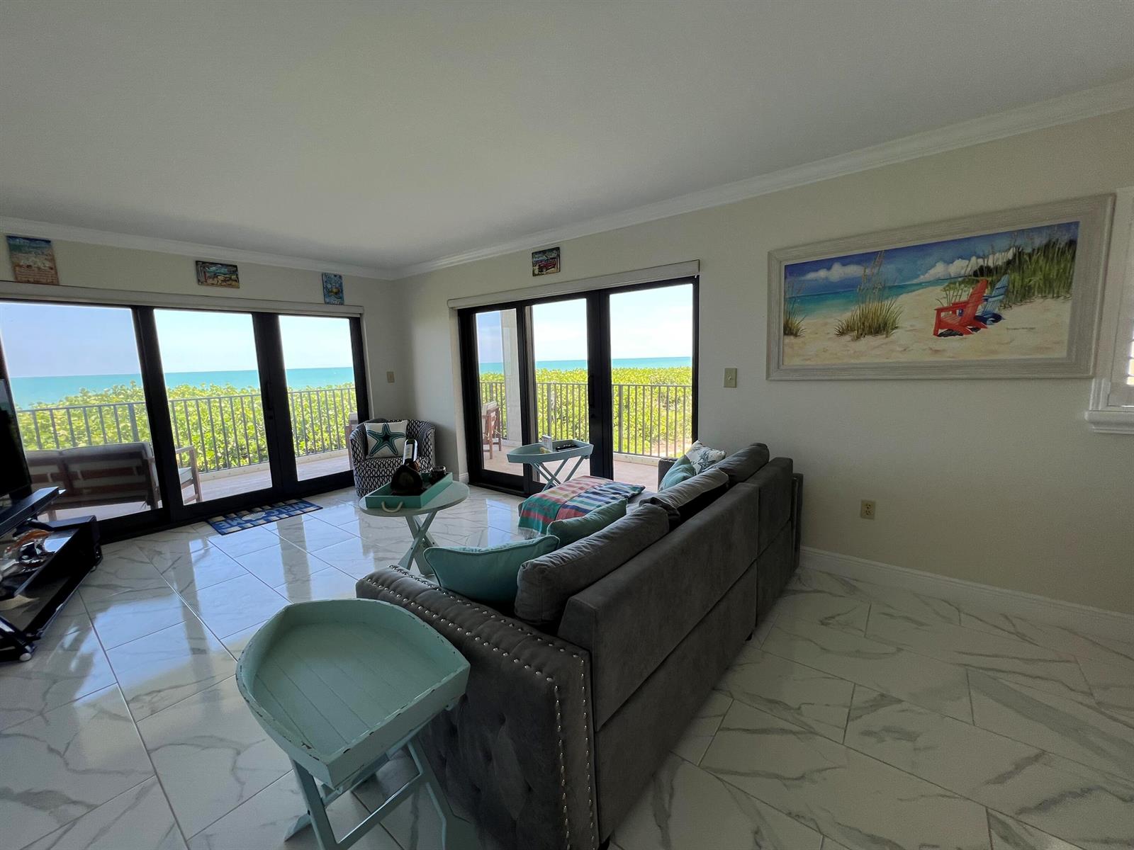 A living room with gray sofa, tile floors, and sliding glass doors overlooking the ocean — 7420 S Ocean Drive # 216, Jensen Beach FL 34957, JENSEN BEACH, FL