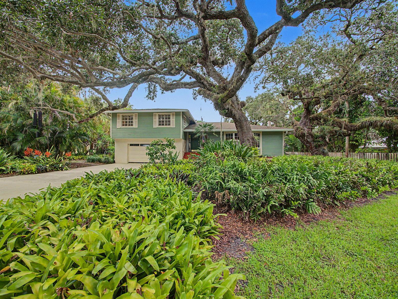 A two-story green house with a garage is surrounded by large trees and lush landscaping — 14 Emarita Way, Sewalls Point FL 34996, SEWALLS POINT, FL