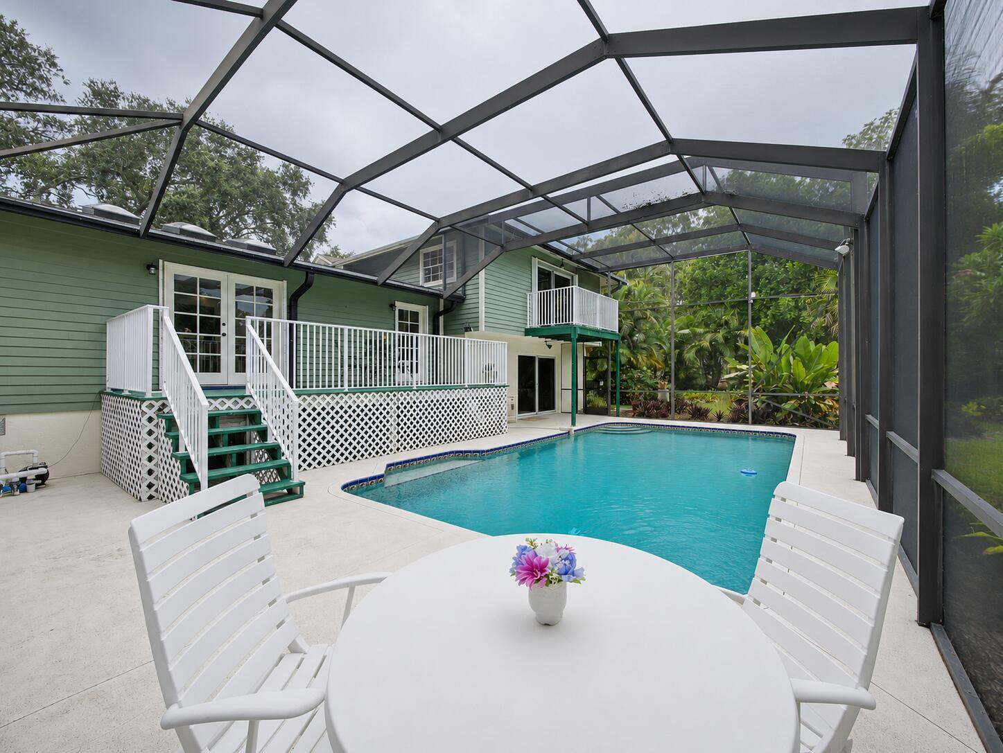 A screened-in pool deck features a white table, two chairs, and a raised wooden deck — 14 Emarita Way, Sewalls Point FL 34996, SEWALLS POINT, FL