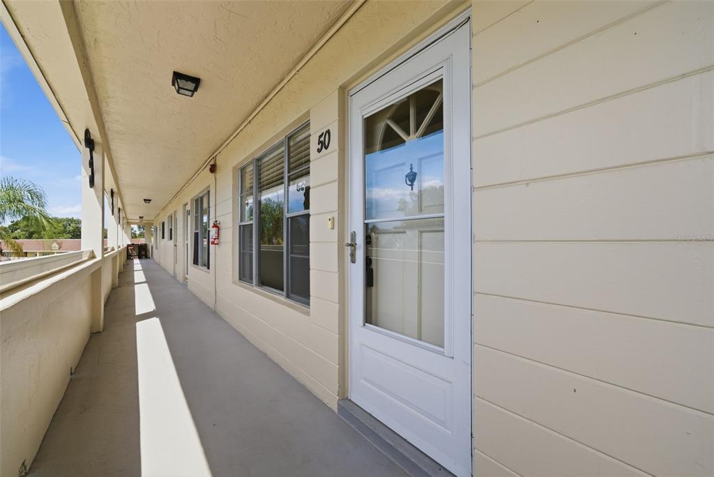 An exterior view of a building walkway with a white door labeled number 50 — 2434 AUSTRALIA WAY E UNIT 50, CLEARWATER, FL
