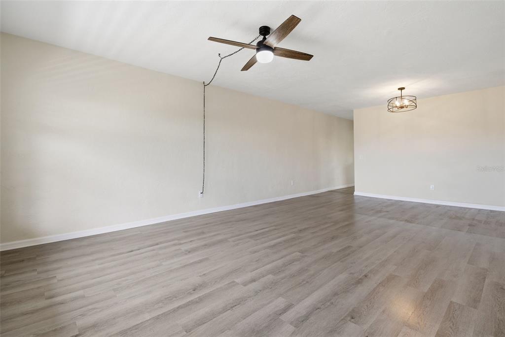 An empty room with light wood-look flooring, beige walls, a ceiling fan, and a chandelier — 2434 AUSTRALIA WAY E UNIT 50, CLEARWATER, FL
