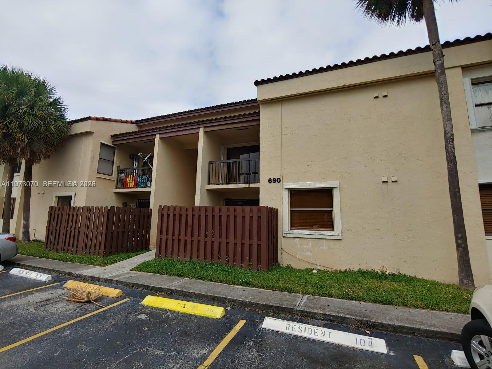 A two-story tan apartment building features brown wooden privacy fences and designated resident parking spaces — 690 W Park Dr # 204, Miami FL 33172, MIAMI, FL
