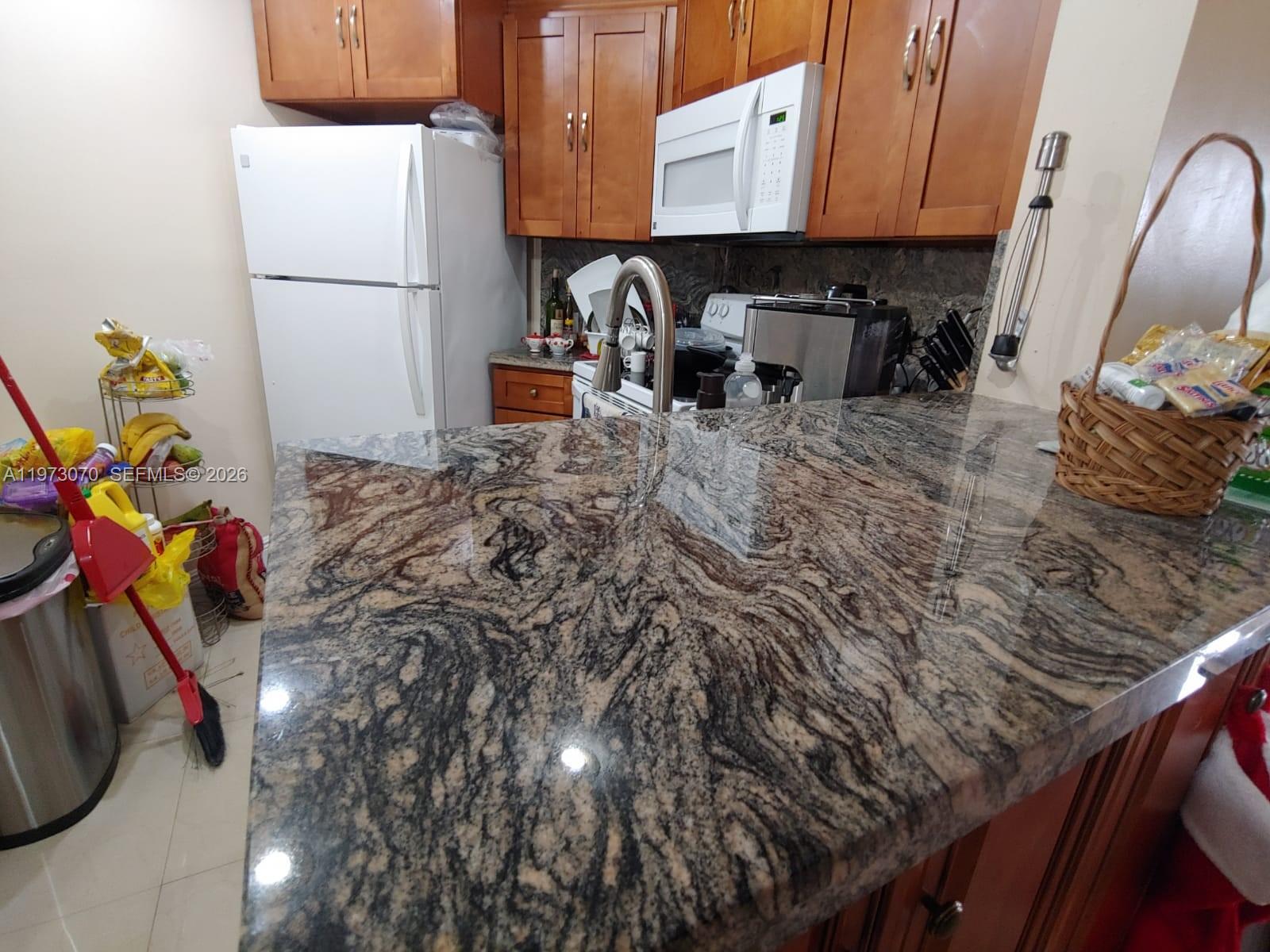 A kitchen features wood cabinets, a white refrigerator, and a polished granite countertop — 690 W Park Dr # 204, Miami FL 33172, MIAMI, FL