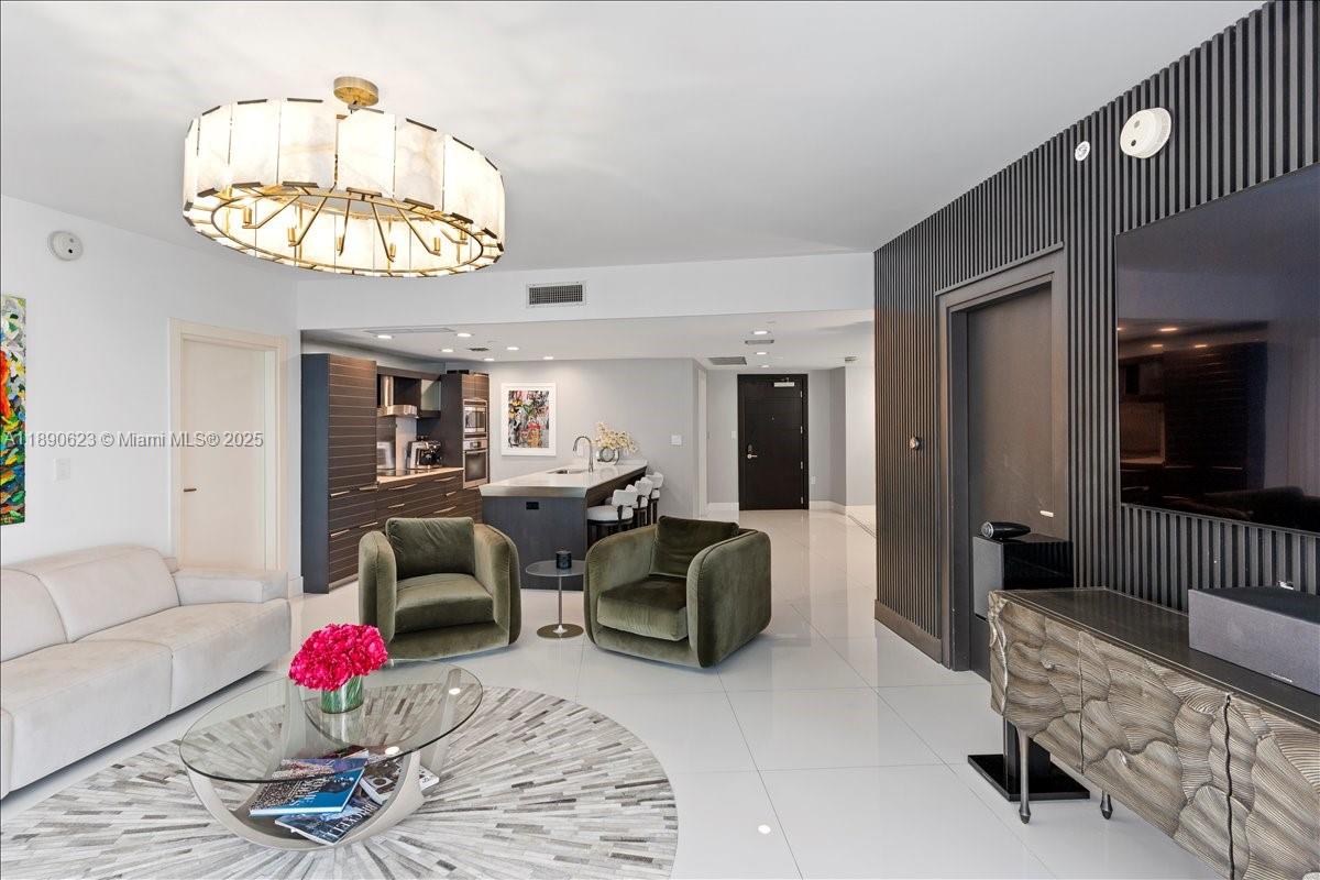 A modern living room features a large chandelier, two green armchairs, and an open kitchen — 200 Biscayne Boulevard Way # 3608, Miami FL 33131, MIAMI, FL