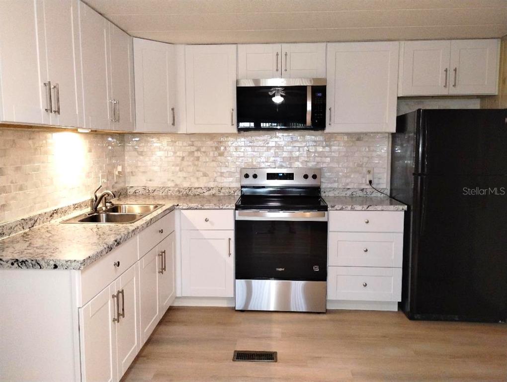 A kitchen features white cabinets, granite countertops, a tiled backsplash, and stainless steel appliances — 9283 DENMARSH DRIVE, BROOKSVILLE, FL