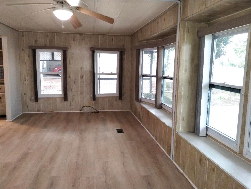 An empty room features wood-paneled walls, light-colored wood flooring, and several windows — 9283 DENMARSH DRIVE, BROOKSVILLE, FL