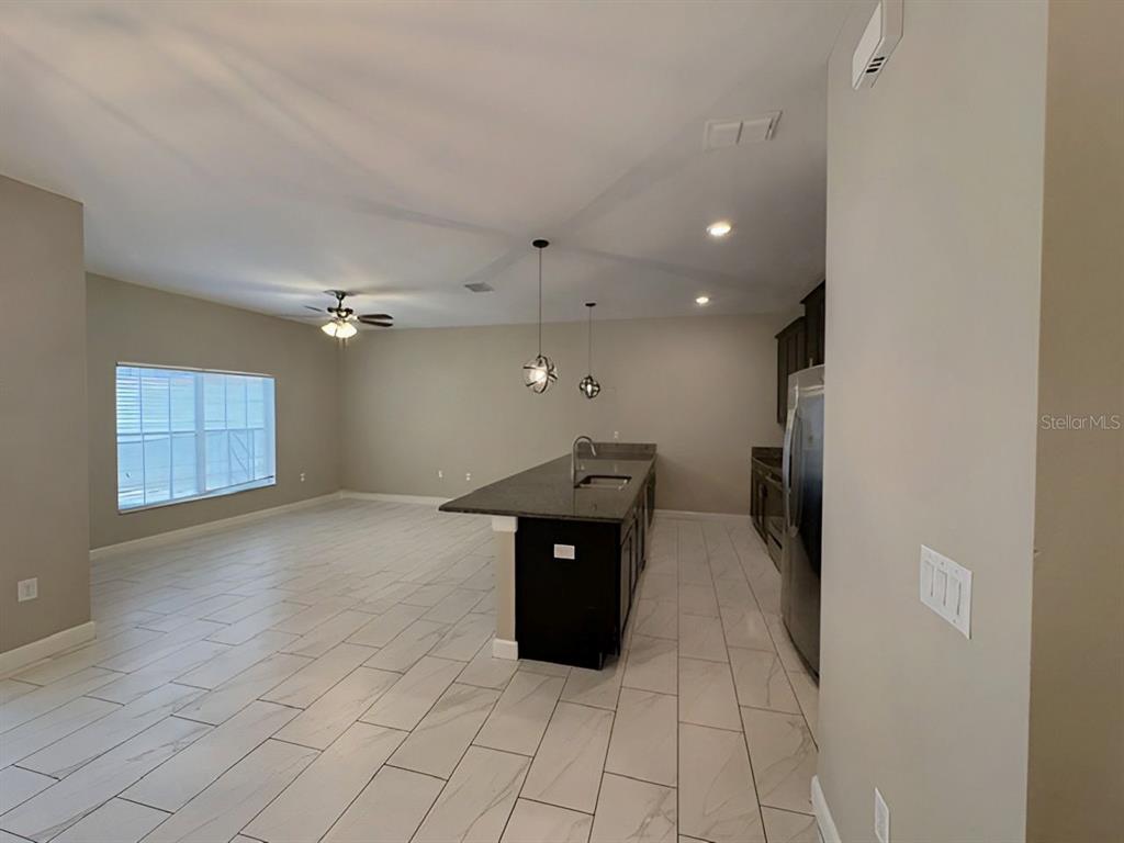 An open-concept kitchen and living area features dark cabinets, a granite island, and tiled floors — 1592 MOON VALLEY DRIVE, DAVENPORT, FL