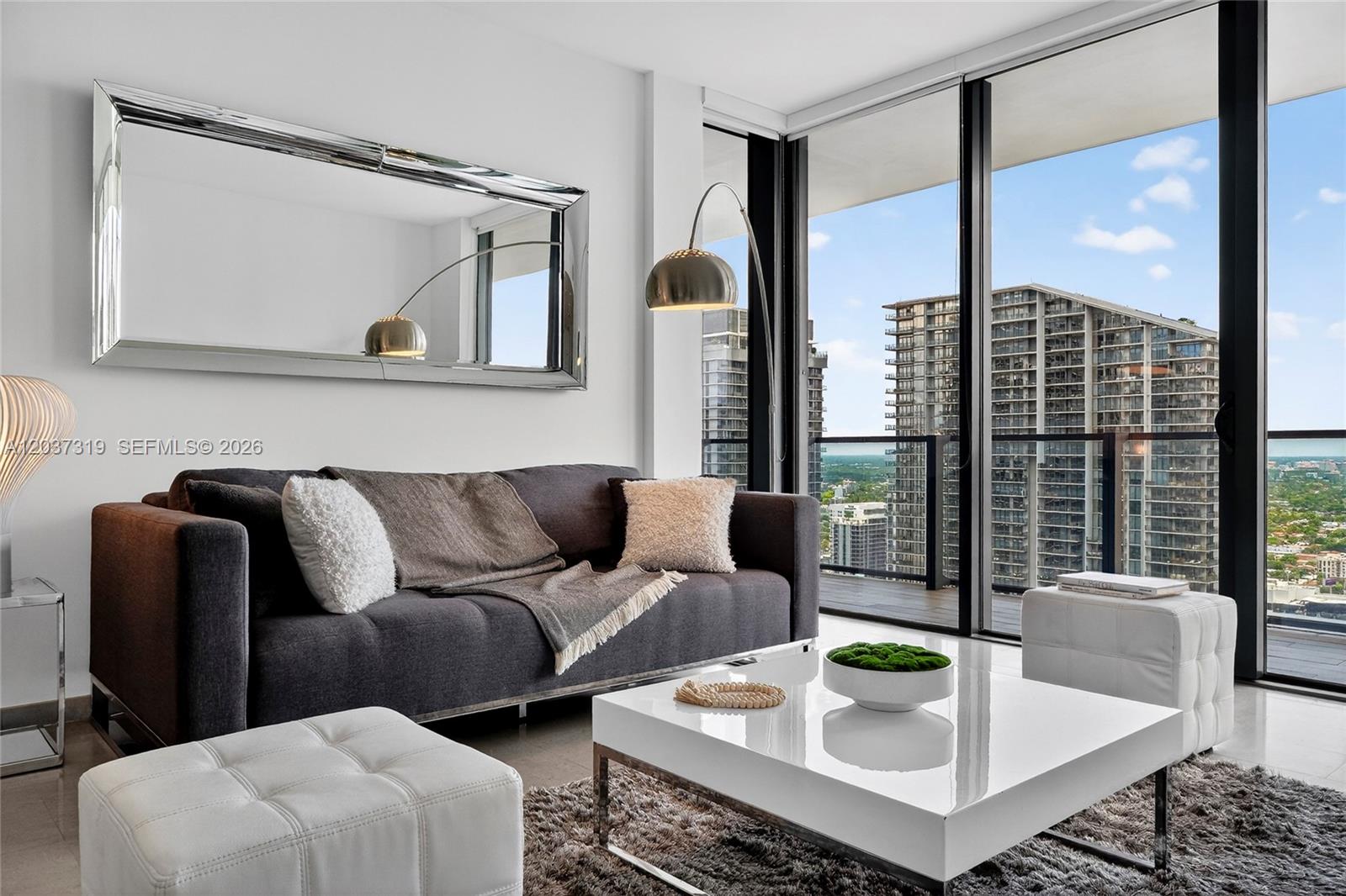 A modern living room features a dark sofa, white coffee table, and floor-to-ceiling windows — 68 SE 6th St # 3506, Miami FL 33131, MIAMI, FL