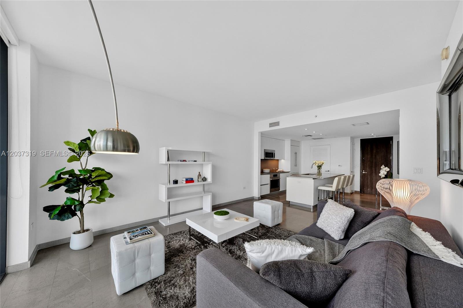A modern living room with a gray sofa, white coffee table, and an open kitchen — 68 SE 6th St # 3506, Miami FL 33131, MIAMI, FL