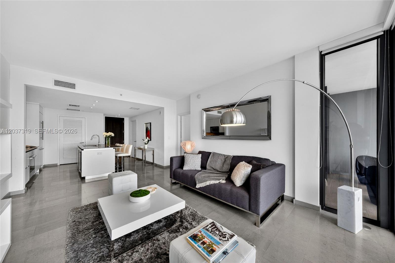 A modern living room features a dark gray sofa, white coffee table, and a floor lamp — 68 SE 6th St # 3506, Miami FL 33131, MIAMI, FL
