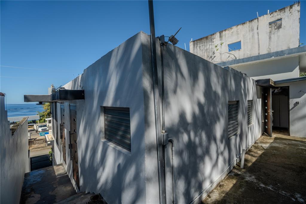 A concrete building exterior with louvered windows and a view of the ocean nearby — 2 BO. BORINQUEN, AGUADILLA, PR