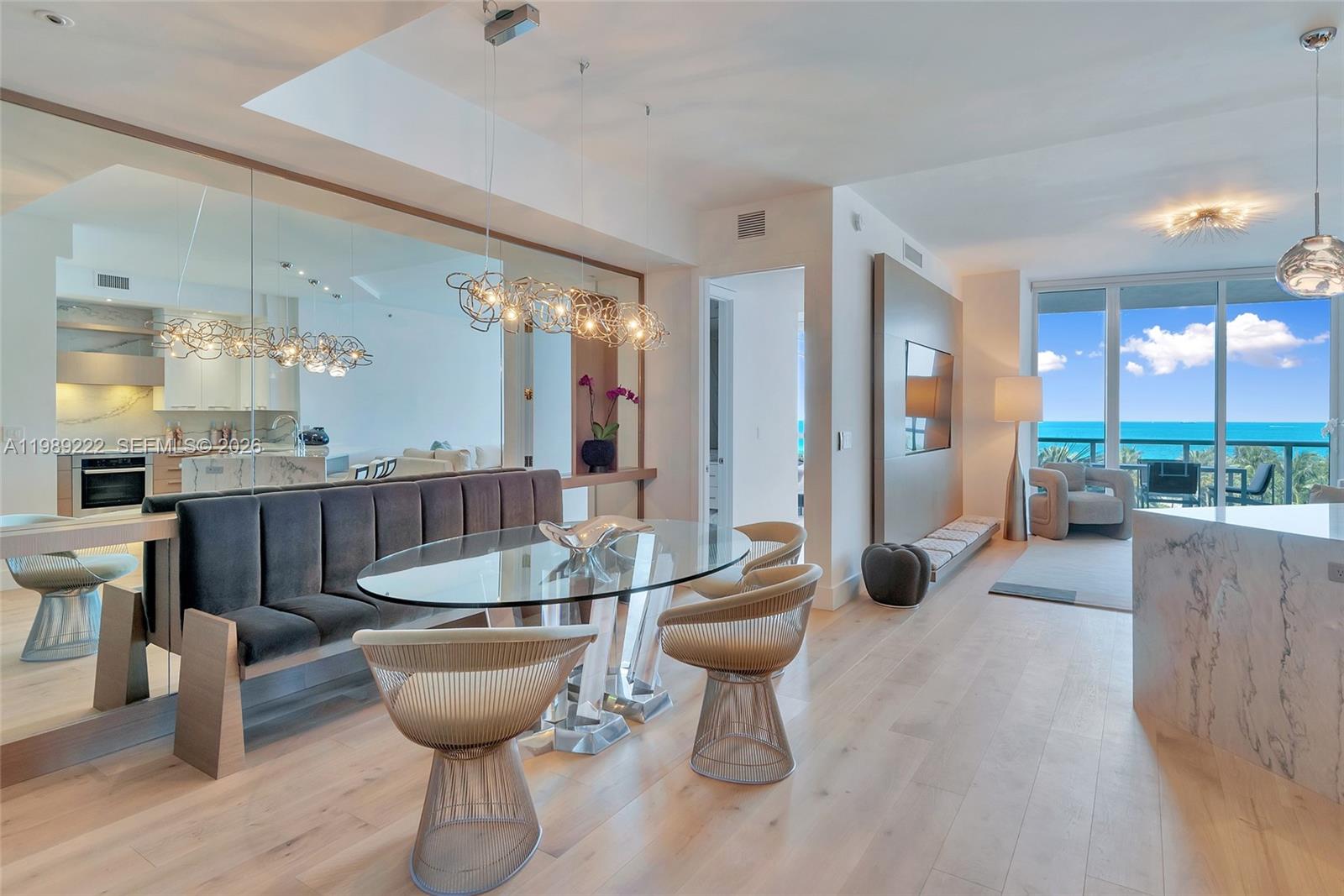 A dining area with a glass table, velvet bench, and ocean view through floor-to-ceiling windows — 100 S Pointe Dr # 708, Miami Beach FL 33139, MIAMI BEACH, FL