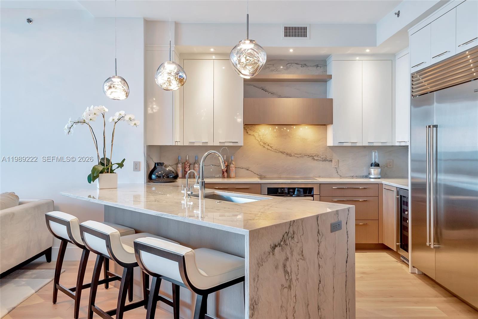 A modern kitchen features a marble waterfall island, white cabinetry, and stainless steel appliances — 100 S Pointe Dr # 708, Miami Beach FL 33139, MIAMI BEACH, FL