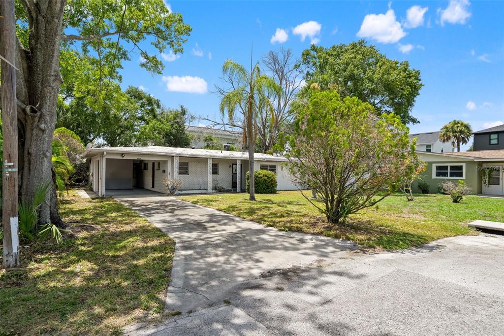 A single-story white brick house with a carport and a concrete driveway under a blue sky — 4635 W BAY VILLA AVENUE, TAMPA, FL