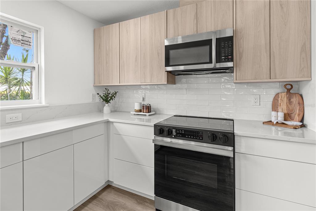 A modern kitchen features white cabinets, light wood upper cabinets, and stainless steel appliances — 2917 W CLIFTON STREET, TAMPA, FL