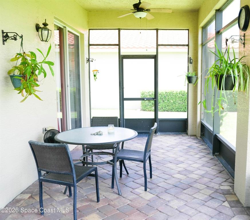 A screened-in patio features a round table, four chairs, hanging plants, and paver flooring — 5566 57TH WAY, VERO BEACH, FL