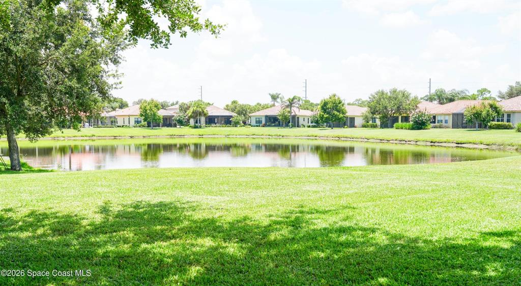 A grassy lawn leads to a pond surrounded by residential houses under a bright sky — 5566 57TH WAY, VERO BEACH, FL