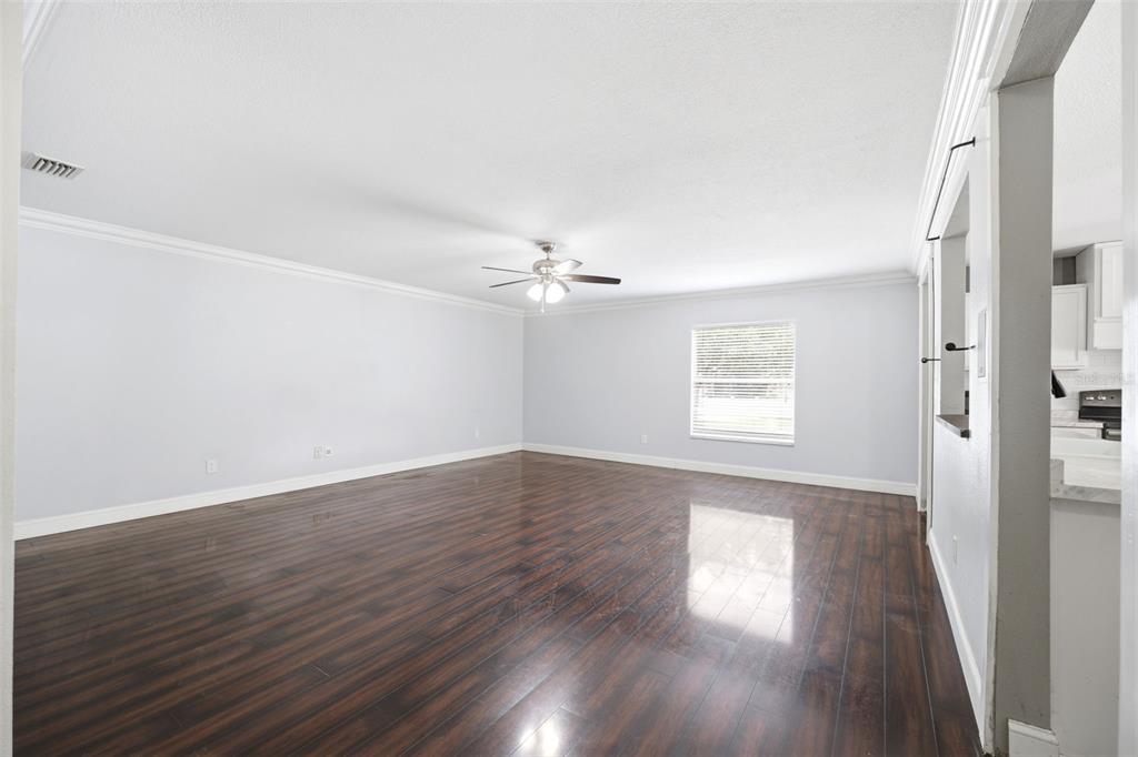 An empty living room features dark wood-look flooring, light gray walls, and a ceiling fan — 14026 JACOBSON DRIVE, ODESSA, FL