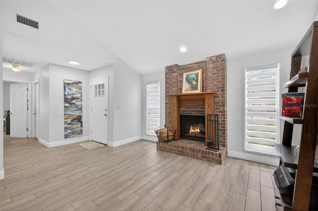 A living room features a brick fireplace, light wood-look tile flooring, and a white door — 11207 FIRESIDE DRIVE, TAMPA, FL