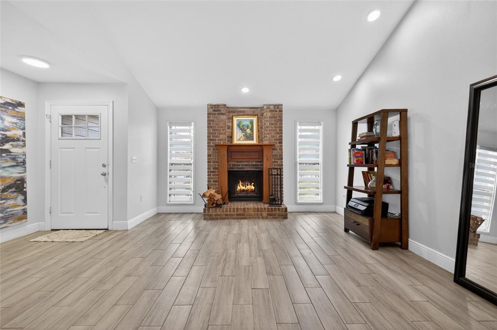 A living room with light wood-look tile flooring, a brick fireplace, and a white door — 11207 FIRESIDE DRIVE, TAMPA, FL