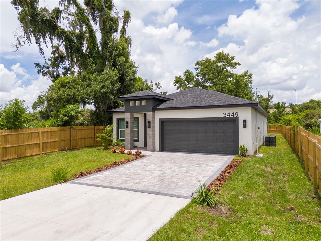 A modern single-story house with a gray garage, paved driveway, and wooden perimeter fencing — 3449 W JEFFERSON STREET, ORLANDO, FL