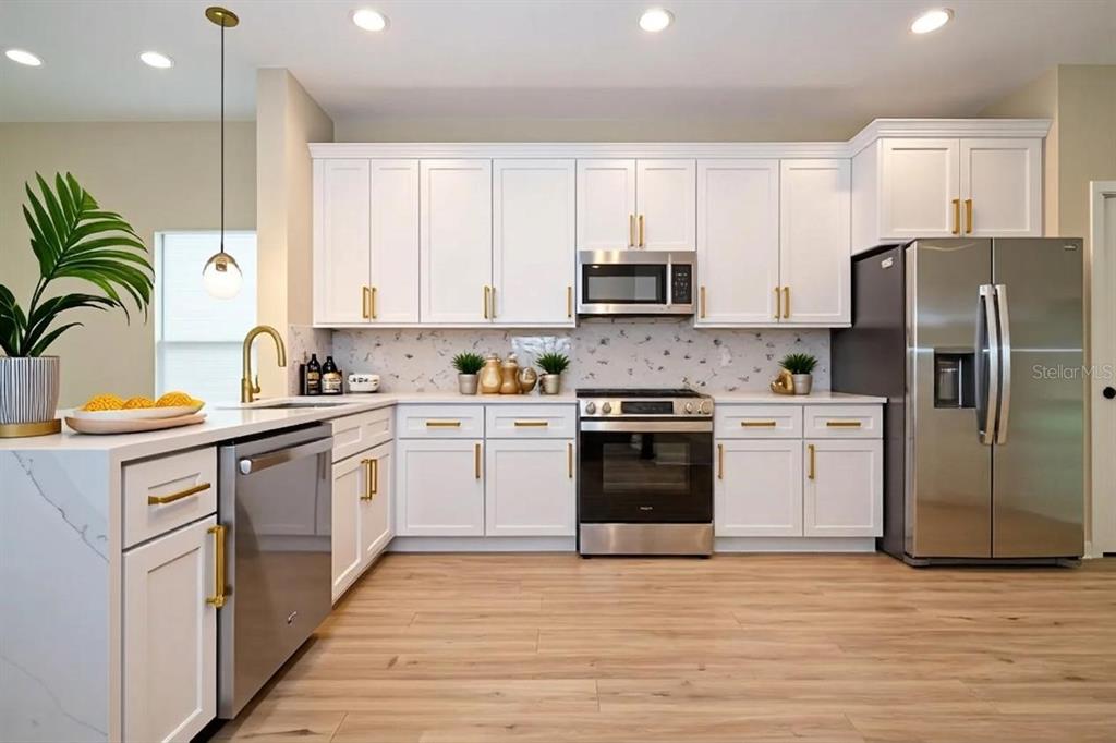 A modern kitchen features white cabinets, stainless steel appliances, gold hardware, and light wood flooring — 3449 W JEFFERSON STREET, ORLANDO, FL