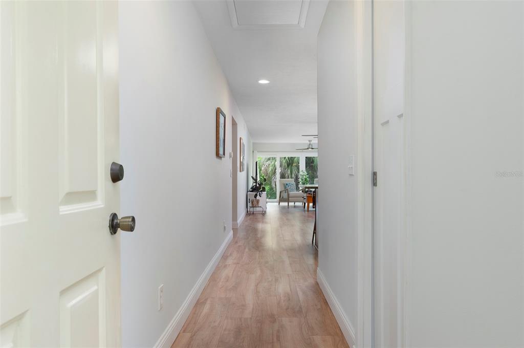 A hallway with light wood-look flooring leads toward a bright living area with large windows — 10152 REGAL DRIVE, LARGO, FL