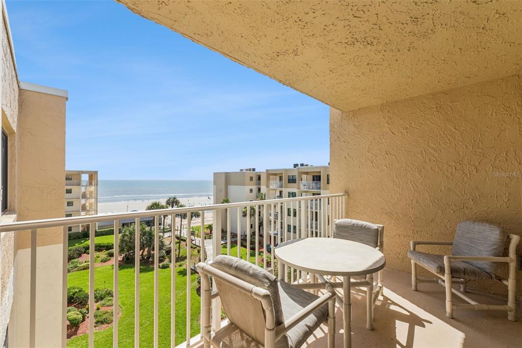 A balcony with a table and chairs overlooks a grassy courtyard and the ocean — 4175 S ATLANTIC AVENUE UNIT 511, NEW SMYRNA BEACH, FL