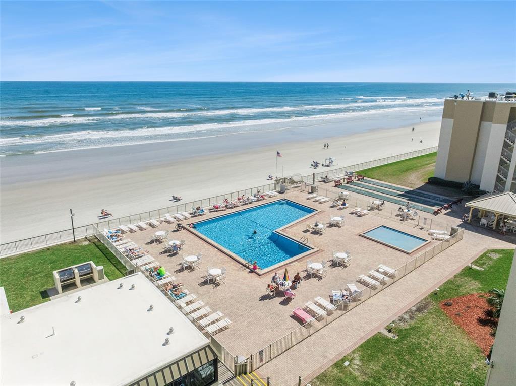 An elevated view of a beachside swimming pool and patio area next to the ocean — 4175 S ATLANTIC AVENUE UNIT 511, NEW SMYRNA BEACH, FL