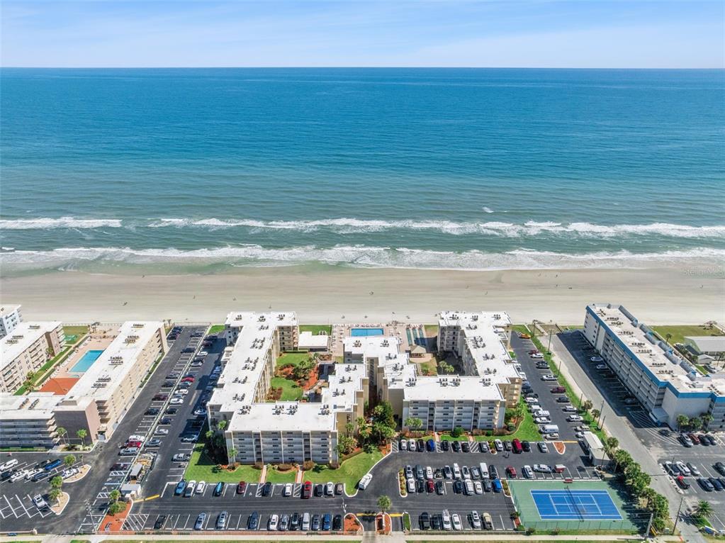 An aerial view shows beachfront apartment complexes with parking lots, a swimming pool, and tennis courts — 4175 S ATLANTIC AVENUE UNIT 511, NEW SMYRNA BEACH, FL