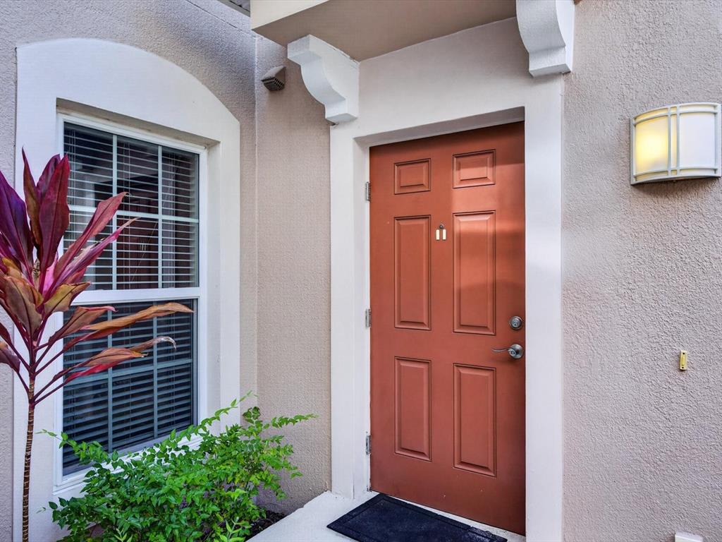 A red front door with a peephole sits next to a window and exterior light — 8311 FOSTER DRIVE, DAVENPORT, FL