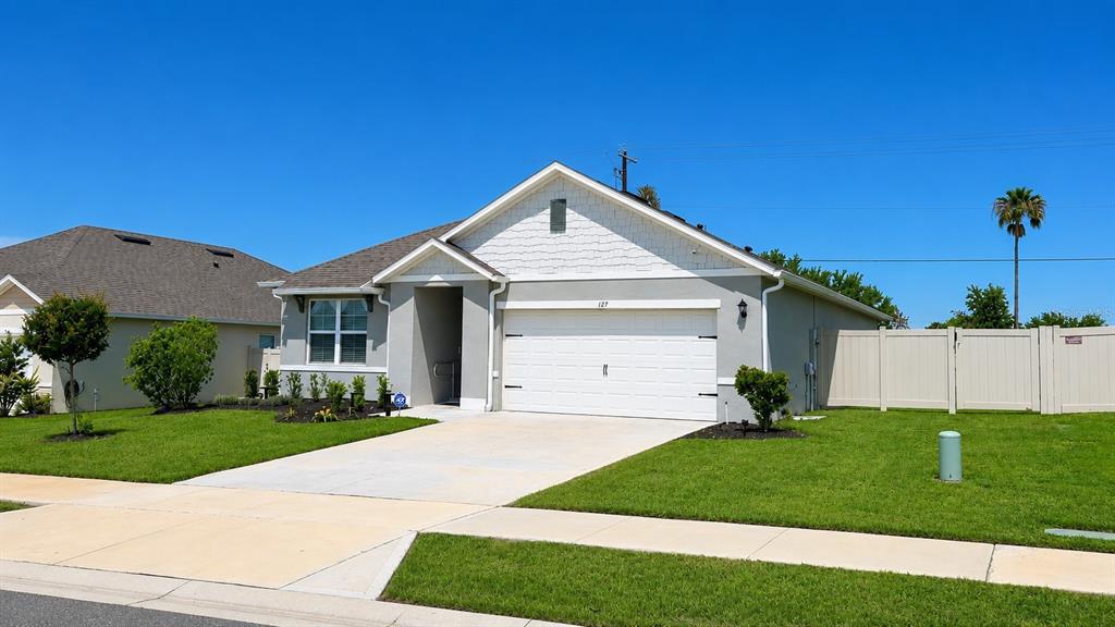 A single-story house with a white garage, gray siding, and a tan fence under blue sky — 127 AUBURN GROVE BOULEVARD, AUBURNDALE, FL