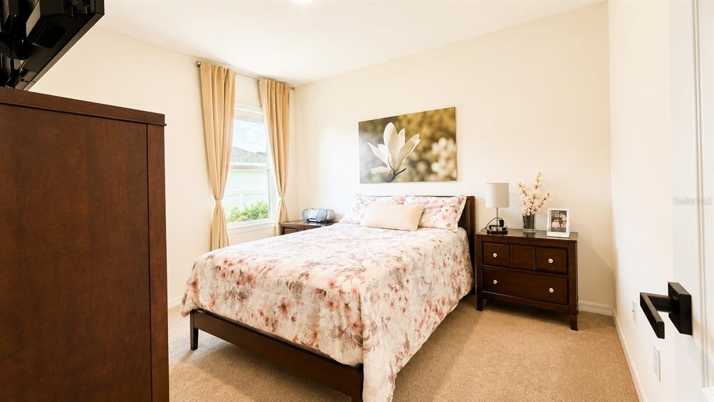 A bedroom features a bed with floral bedding, a dark wood nightstand, and a window — 127 AUBURN GROVE BOULEVARD, AUBURNDALE, FL
