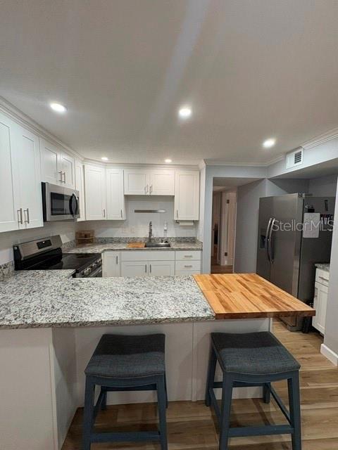 A kitchen features white cabinets, granite countertops, a wooden breakfast bar, and stainless steel appliances — 2302 S MANHATTAN AVENUE UNIT 215, TAMPA, FL