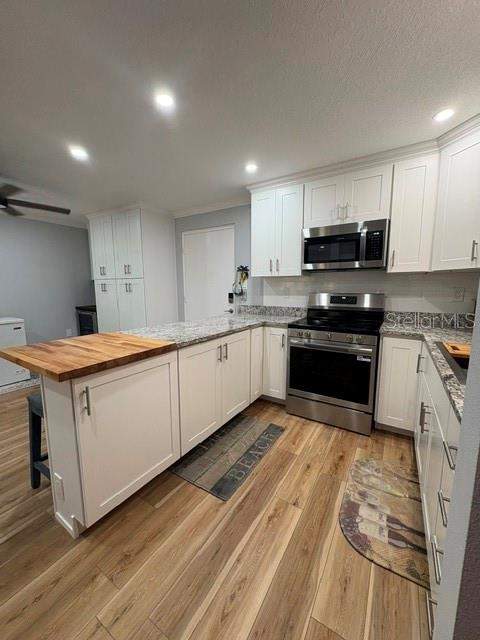 A kitchen features white cabinets, stainless steel appliances, a wood-topped island, and wood-look flooring — 2302 S MANHATTAN AVENUE UNIT 215, TAMPA, FL