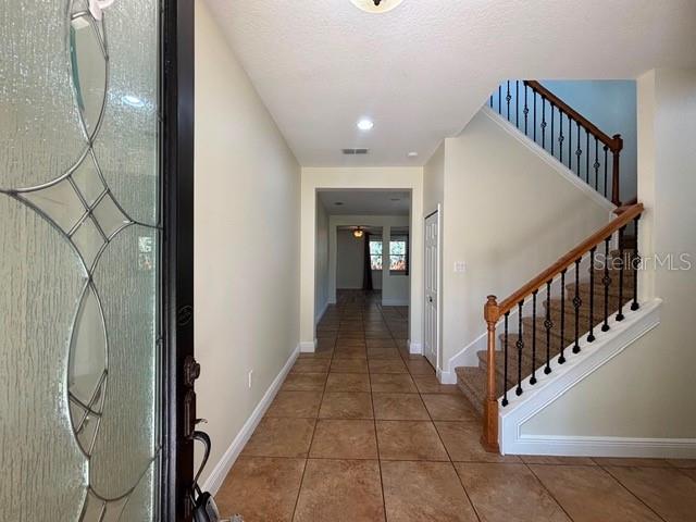 A foyer with tile flooring leads to a staircase with a wooden handrail and metal balusters — 11844 CHATEAUBRIAND AVENUE, ORLANDO, FL