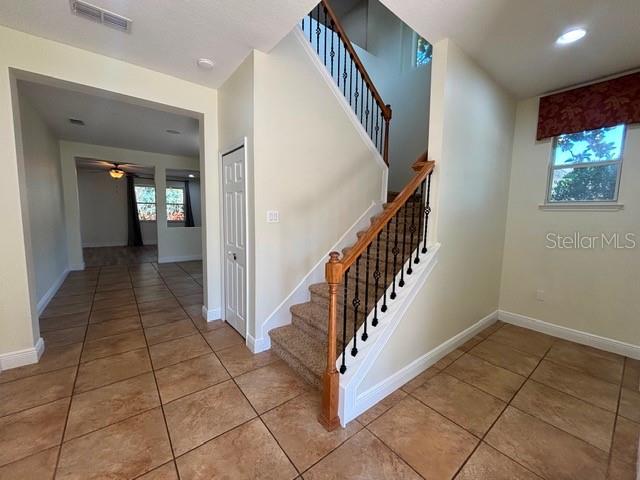 An interior view shows a tiled entryway with a staircase featuring wood railings and carpet — 11844 CHATEAUBRIAND AVENUE, ORLANDO, FL
