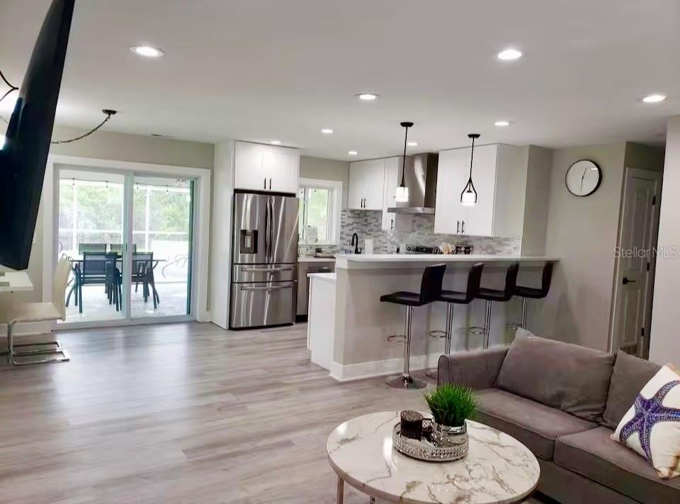 An open-concept kitchen and living area features white cabinets, stainless appliances, and wood-look flooring — 1385 HARMONY DRIVE, PORT CHARLOTTE, FL