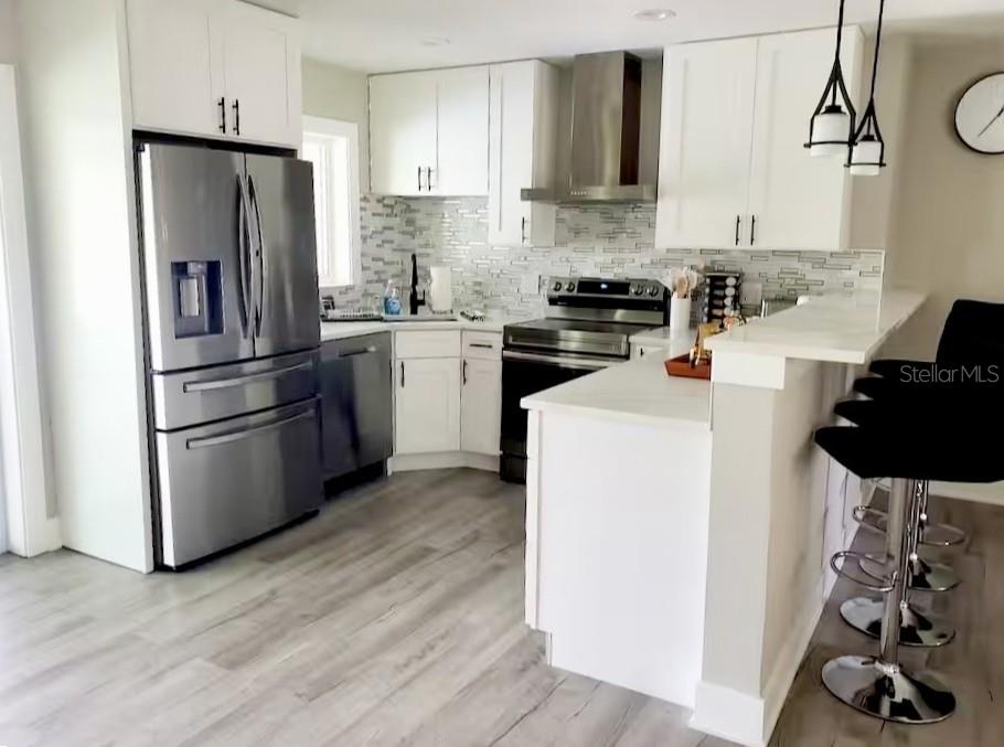 A kitchen with white cabinets, stainless steel appliances, a breakfast bar, and light wood flooring — 1385 HARMONY DRIVE, PORT CHARLOTTE, FL