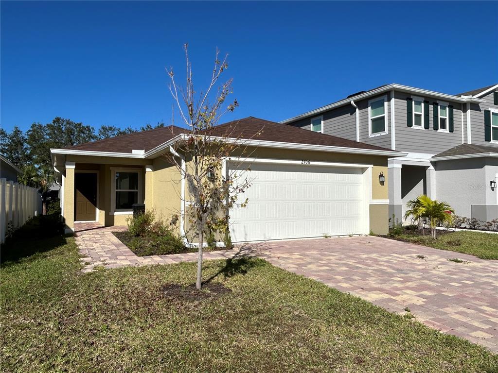 A single-story house with a tan stucco exterior, a two-car garage, and a paver driveway — 2706 89TH STREET CIRCLE E, PALMETTO, FL