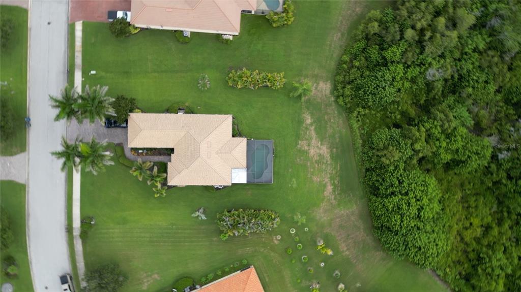 An aerial view shows a house with a pool and a large backyard near woods — 625 148TH COURT NE, BRADENTON, FL