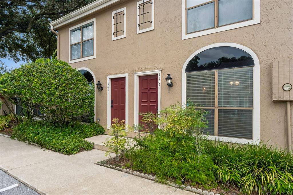 The exterior of a two-story tan stucco building features two red front doors and landscaping — 1307 PARK VILLA PLACE, WINTER SPRINGS, FL