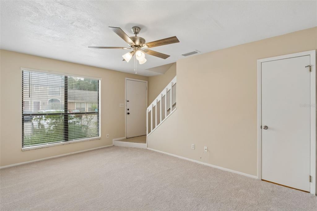 A carpeted living room features a ceiling fan, a large window, and a staircase — 1307 PARK VILLA PLACE, WINTER SPRINGS, FL