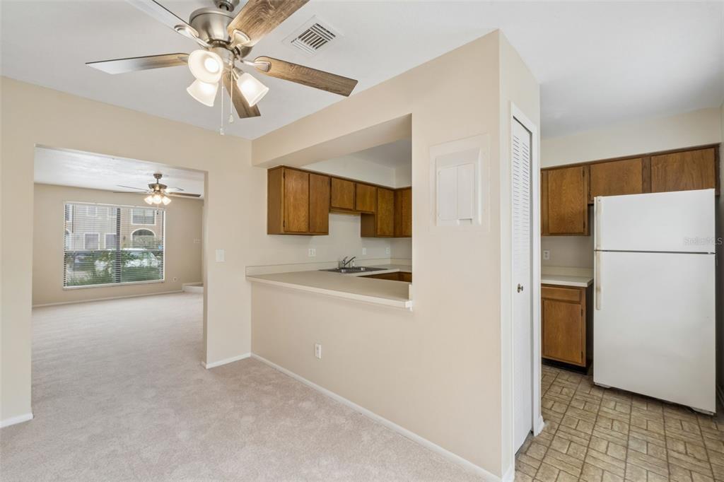 A kitchen with wood cabinets and a white refrigerator overlooks a carpeted dining area — 1307 PARK VILLA PLACE, WINTER SPRINGS, FL