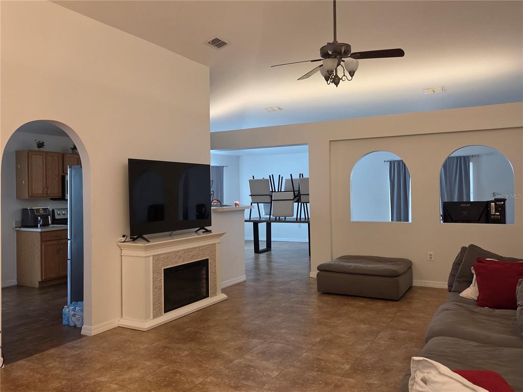 A living room features a fireplace, a television, arched wall openings, and tile flooring — 2215 KINGSCREST CIRCLE, APOPKA, FL