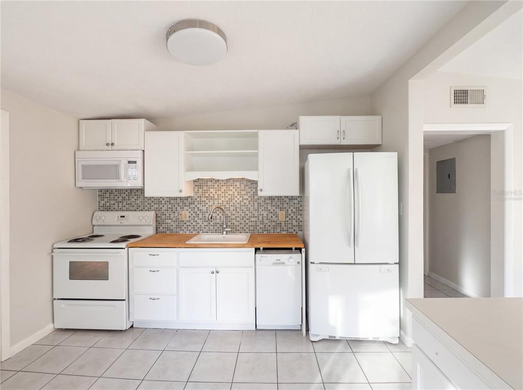 A kitchen with white cabinets, wood countertops, a tiled backsplash, and white appliances — 911 NEW YORK STREET, EDGEWATER, FL